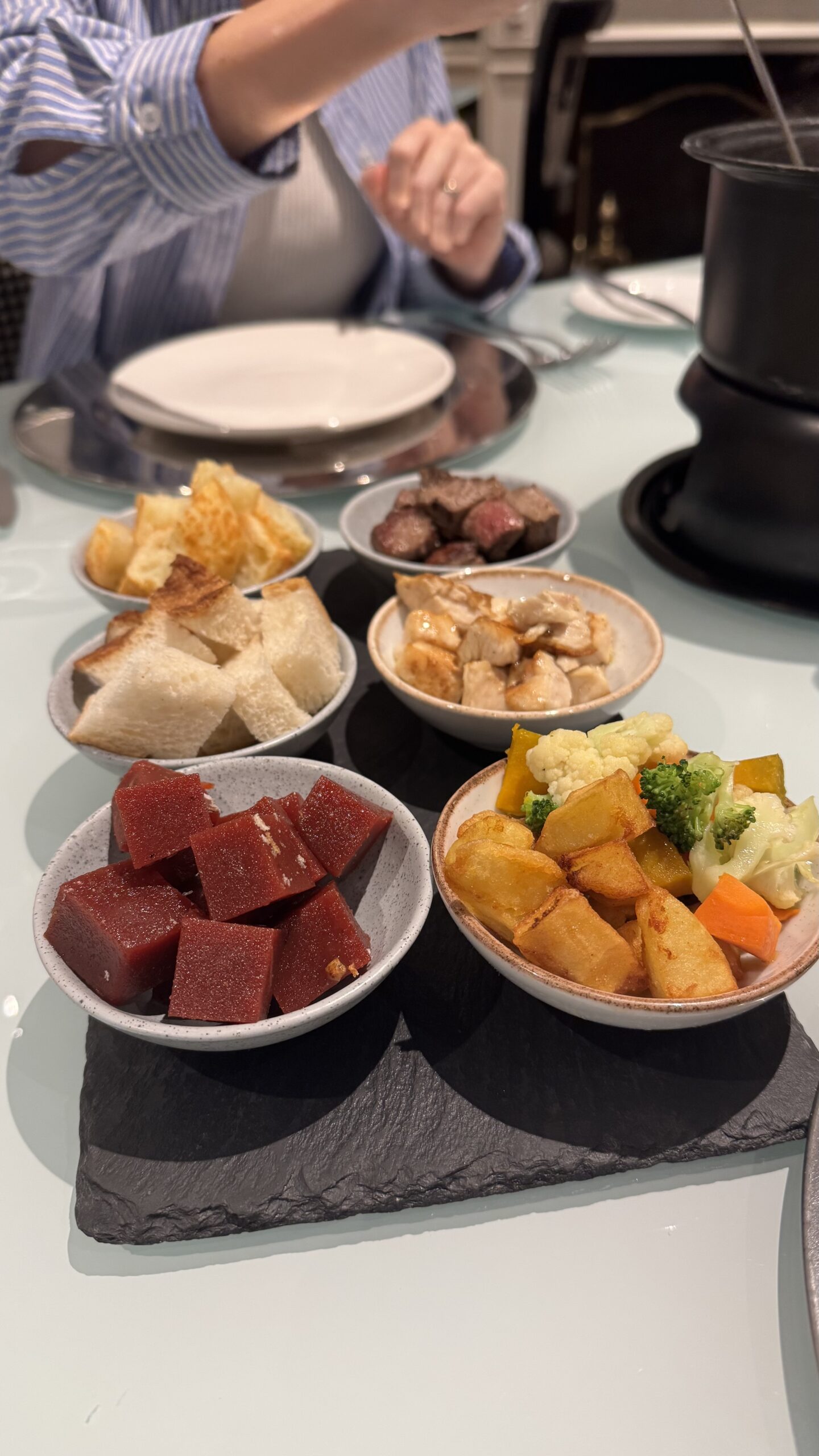 Mesa do fondue de queijo no Grand Mercure Ibirapuera com tigelas de acompanhamentos: carne, frango, vegetais, pão e goiabada