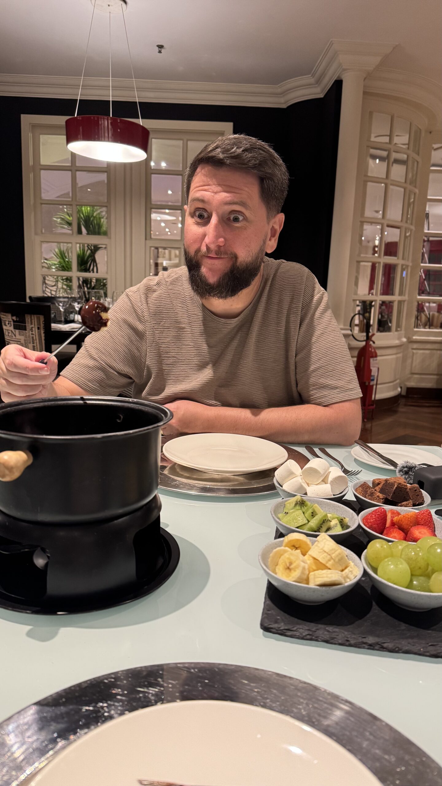 Rudi comendo fondue de chocolate no Grand Mercure Ibirapuera com tigelas de uva, kiwi, morango e marshmallow