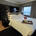 Cama king size da suíte executiva Trousseau no Pullman Ibirapuera com bandeja de chocolates Dengo e rosas da experiência romântica ALL Accor