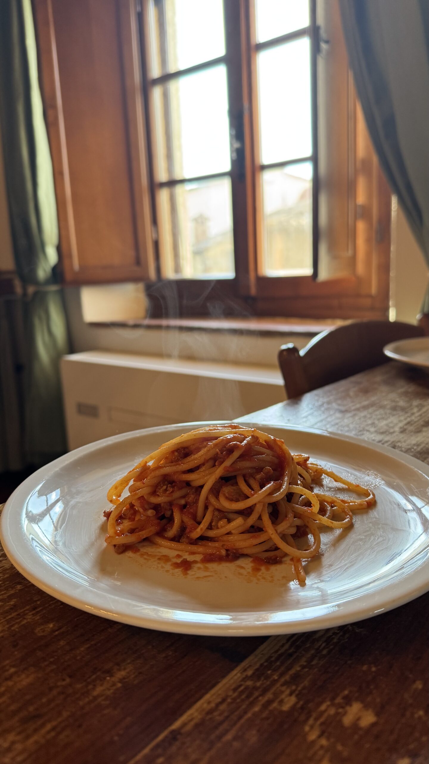 Macarrão caseiro servido em prato branco na mesa de madeira do apartamento na Toscana