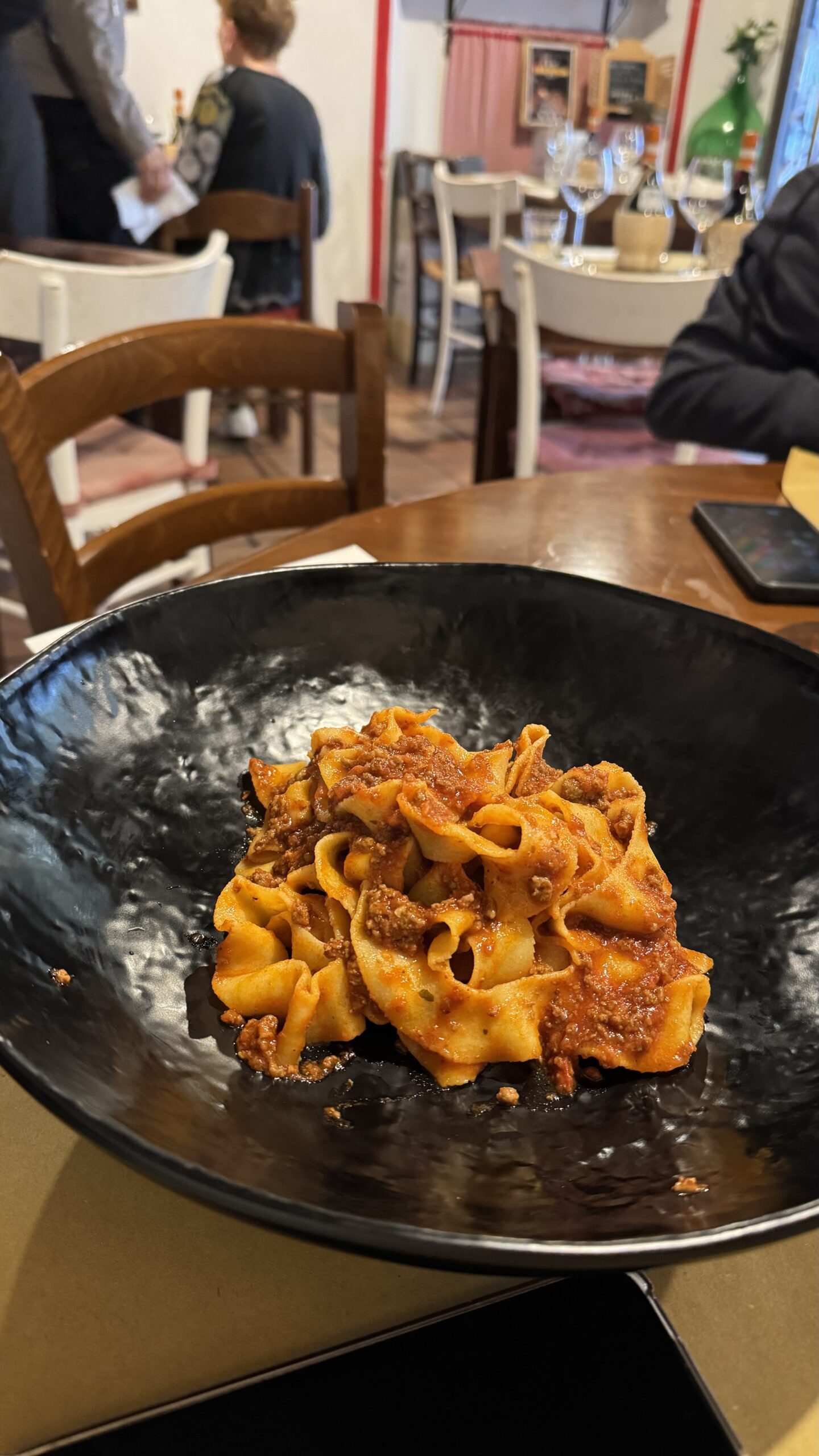 Pappardelle com bolognesa servido em prato preto no restaurante La Bottega del Borgo