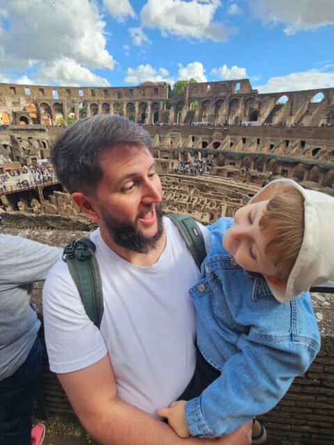 Rudi carregando Sam dentro do Coliseu com a arena ao fundo