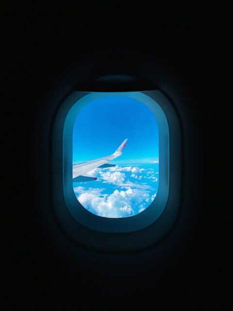 Asa de avião vista pela janela do avião, sobrevoando nuvens em céu azul