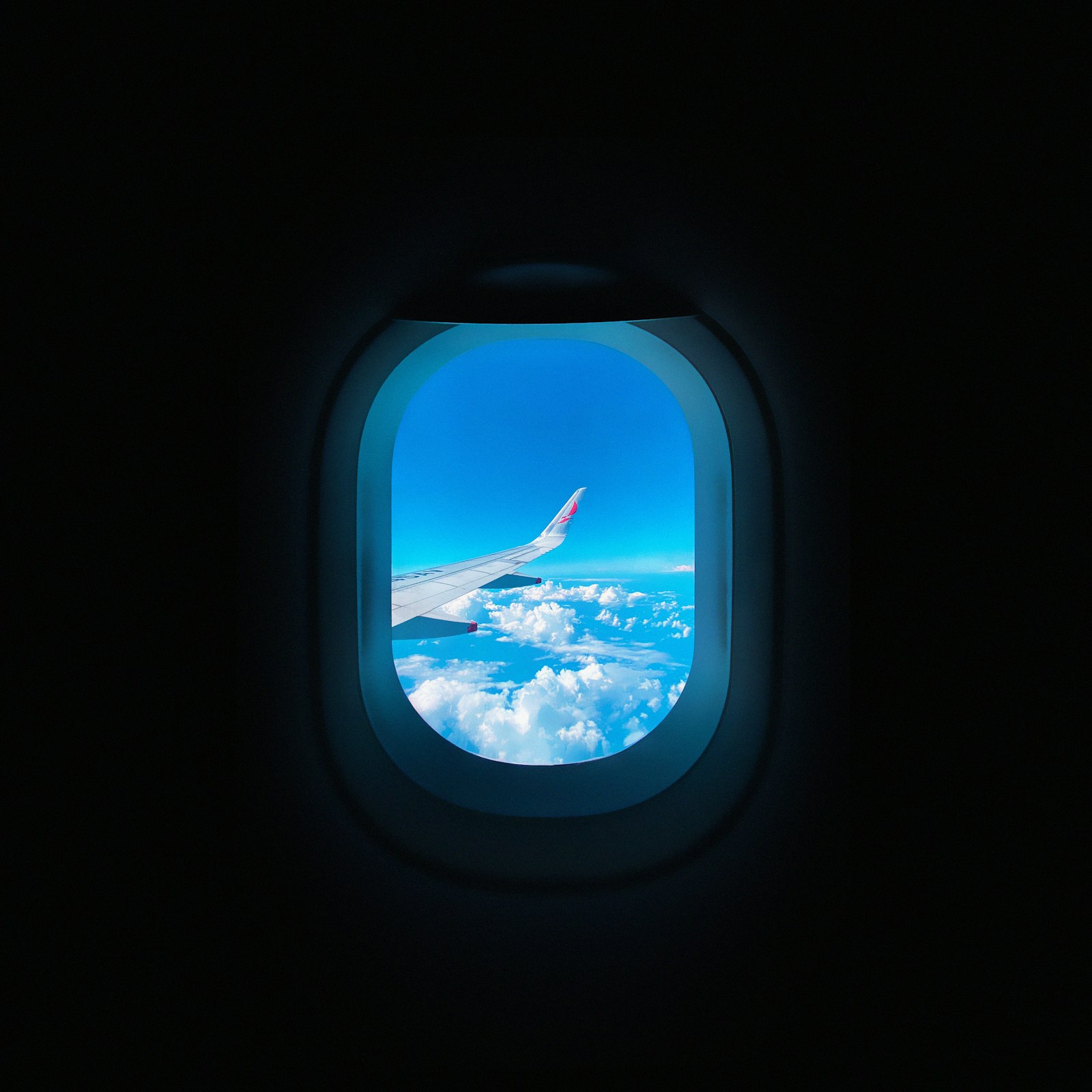 Asa de avião vista pela janela do avião, sobrevoando nuvens em céu azul