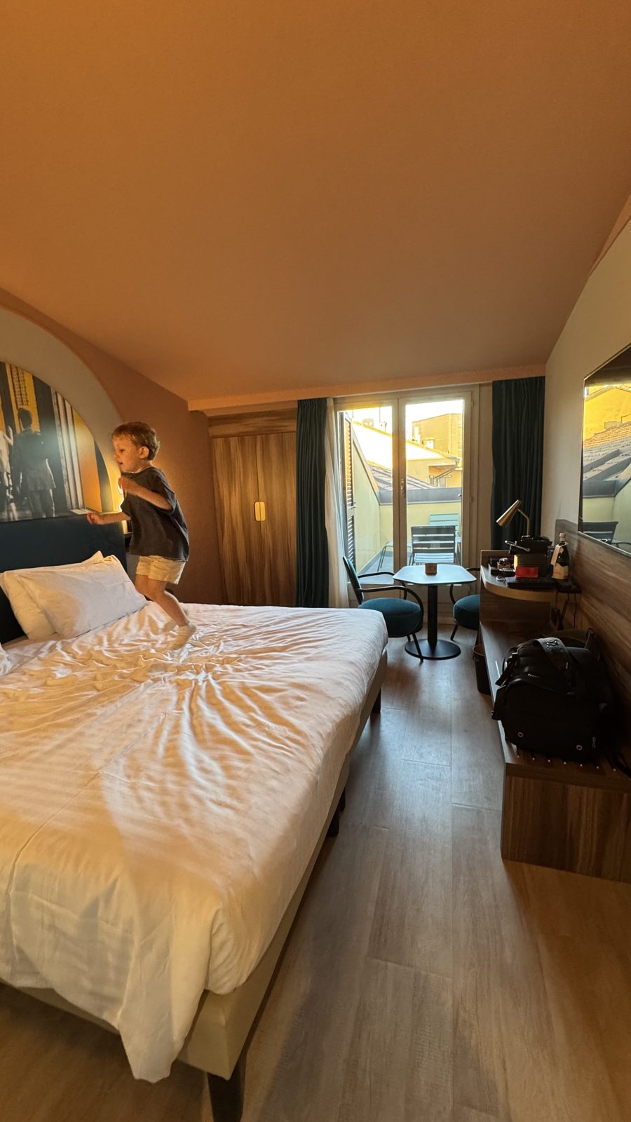Samuel pulando na cama do quarto do Mercure Bologna Central com cabeceira azul