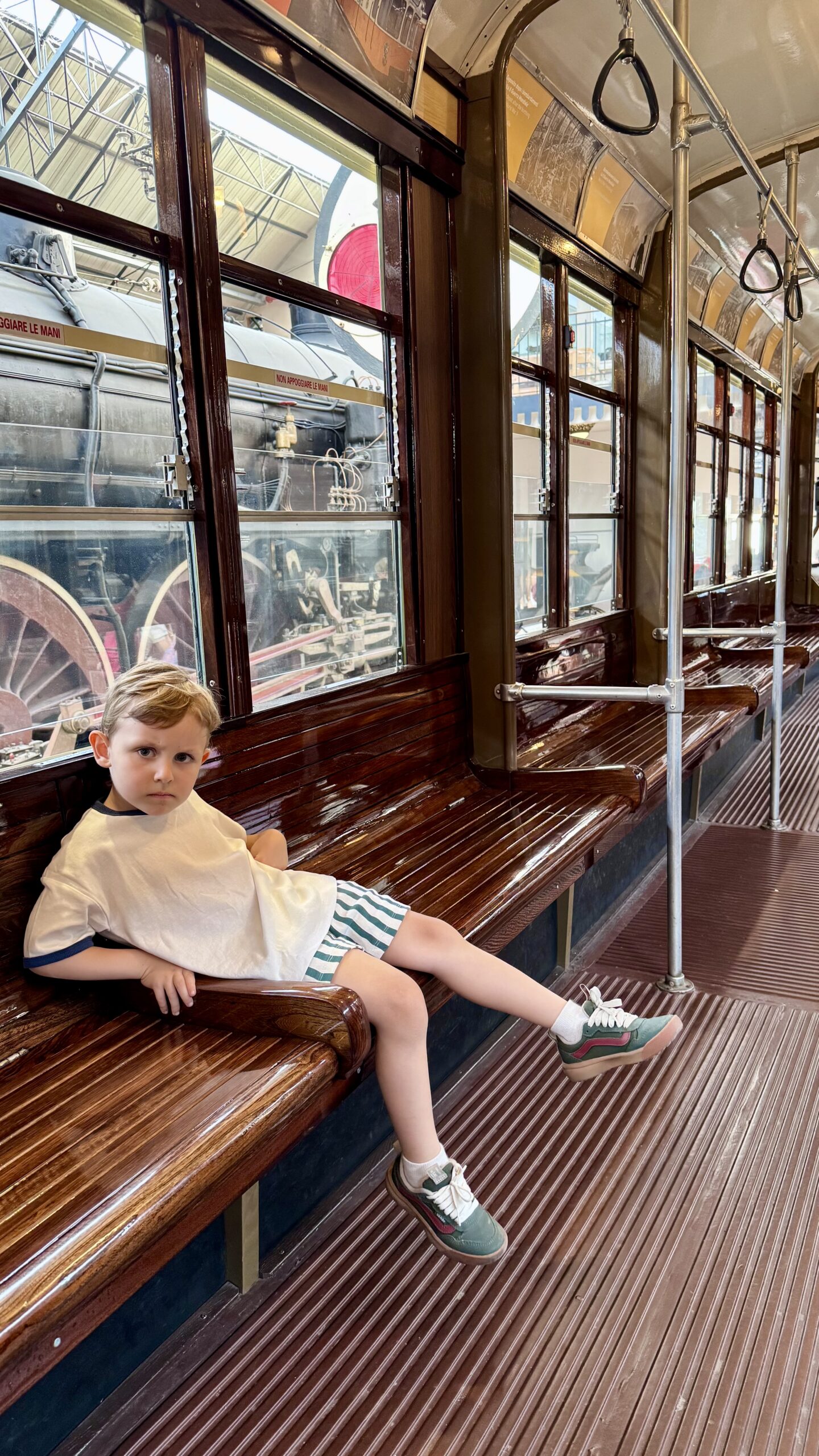 Criança sentado dentro de um bondinho antigo, ao lado das locomotivas no Museu Leonardo da Vinci