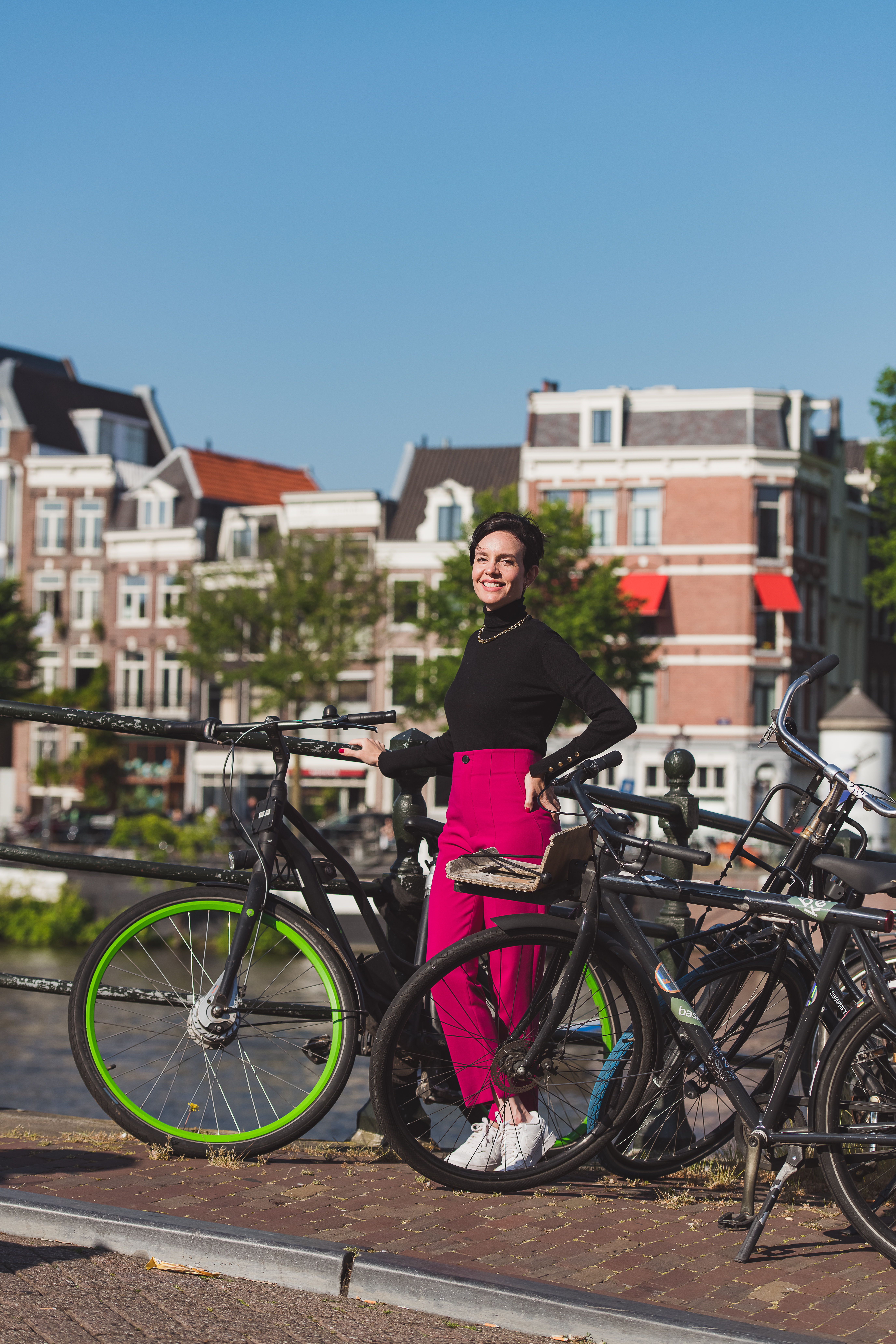Família posando em uma ponte cercada de bicicletas com casas flutuantes e um canal de Amsterdã ao fundo