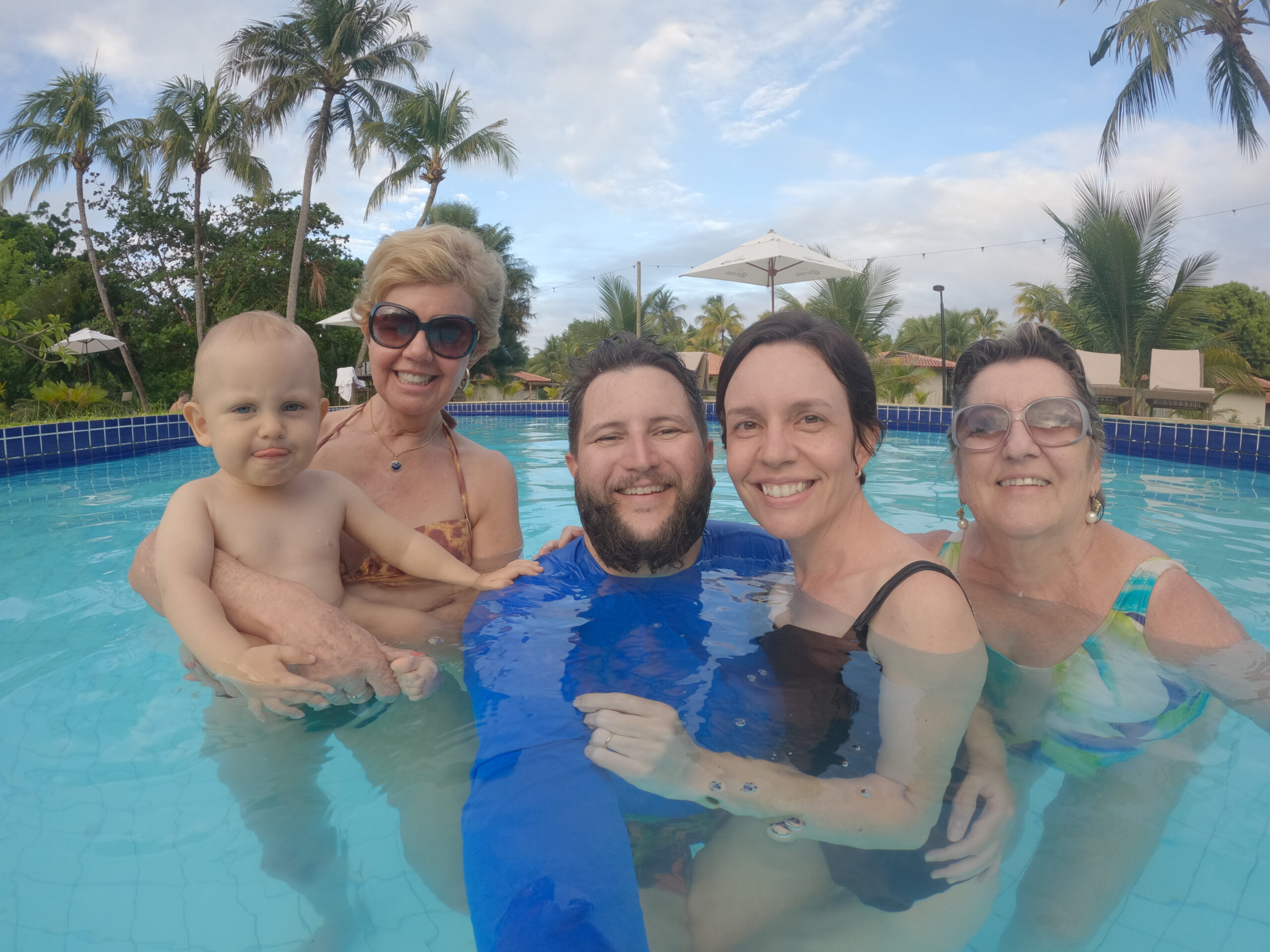 Família reunida em três gerações na piscina do Angá Hotel com coqueiros ao fundo