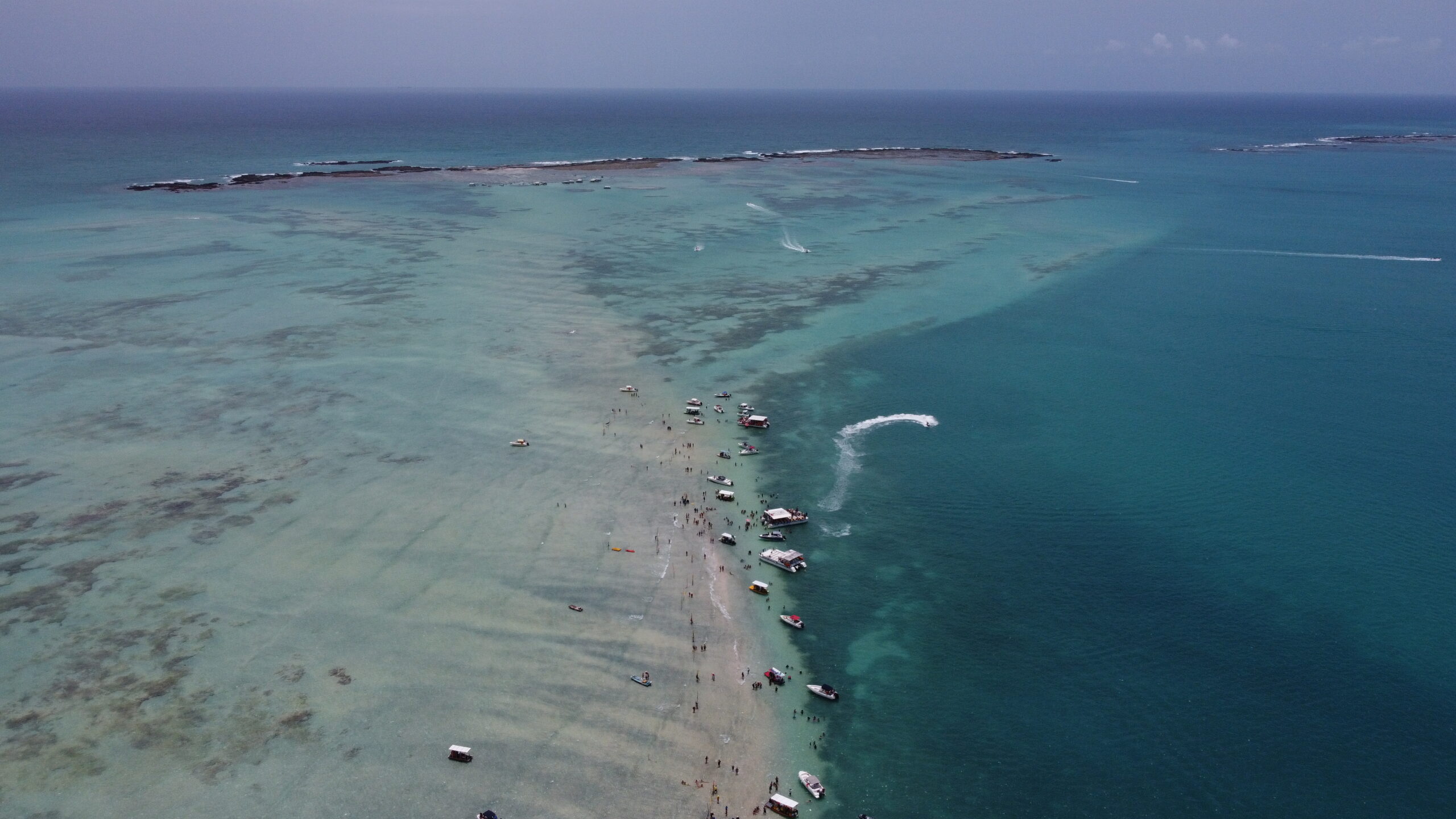 Vista aérea de drone do final do percurso do Caminho de Moisés, com vários barcos e uma moto aquática reunidos perto dos recifes.