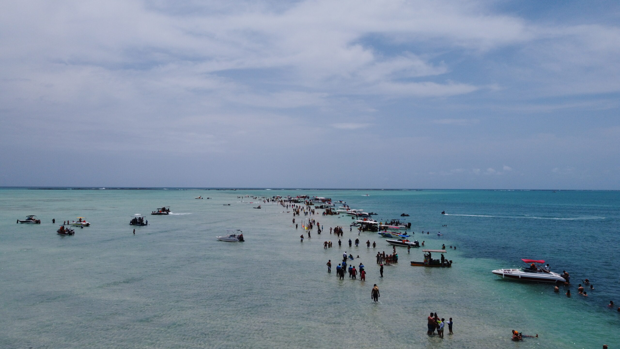 Vista aérea de drone de turistas caminhando em fila pelo banco de areia do Caminho de Moisés na maré baixa, cercados de barcos.