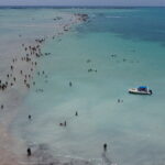 Vista aérea de drone do Caminho de Moisés em Barra Grande, Maragogi, com faixa de areia exposta na maré baixa e lancha ancorada ao lado.