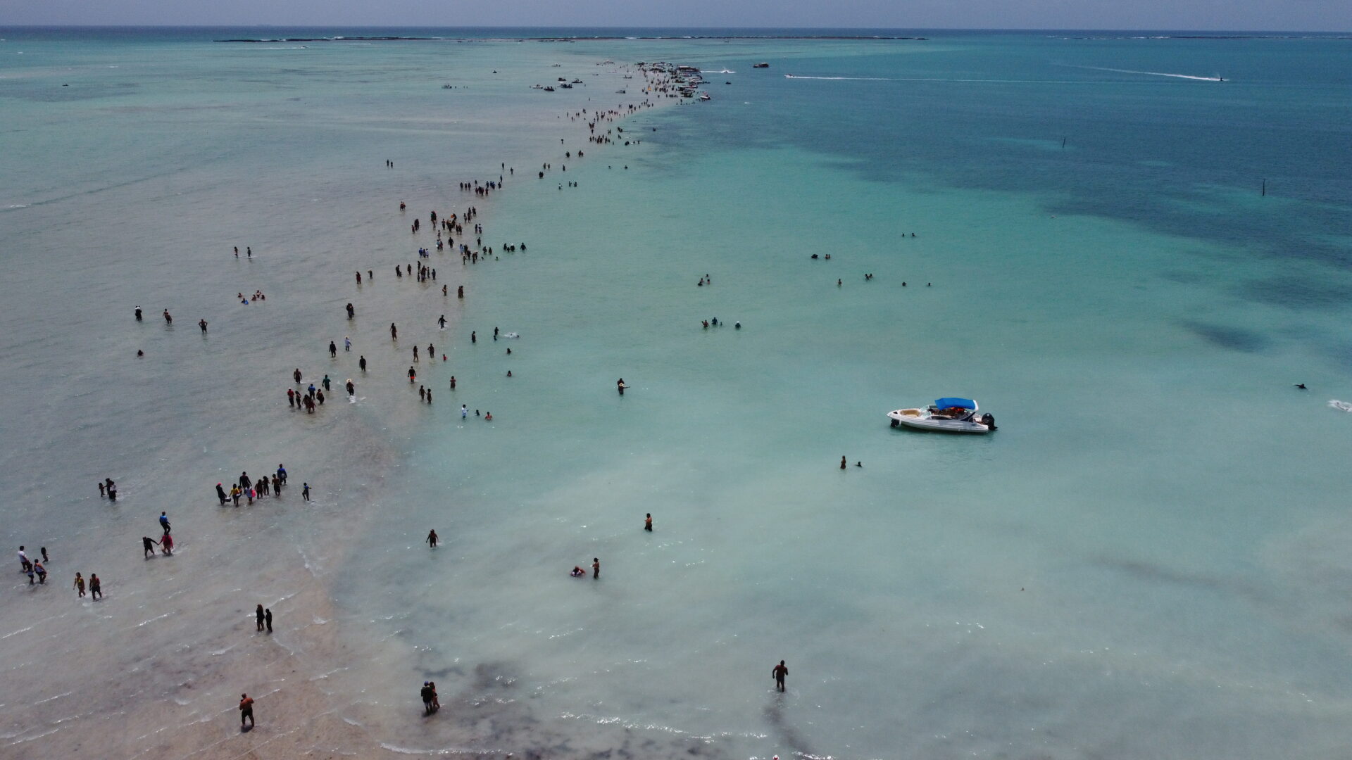 Vista aérea de drone do Caminho de Moisés em Barra Grande, Maragogi, com faixa de areia exposta na maré baixa e lancha ancorada ao lado.
