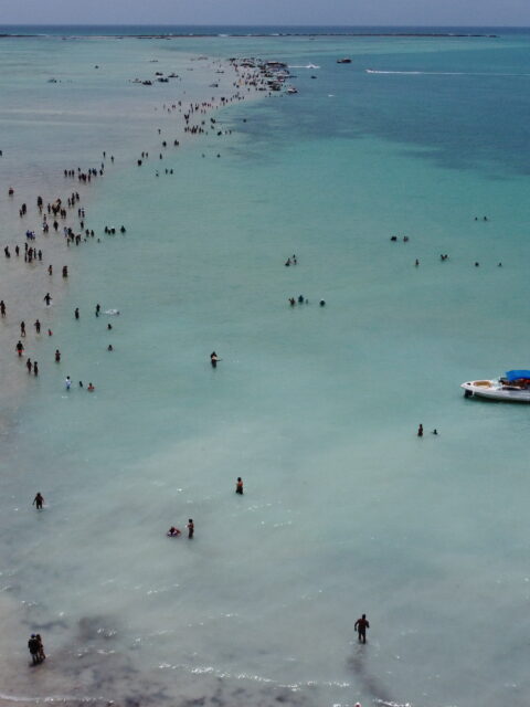 Vista aérea de drone do Caminho de Moisés em Barra Grande, Maragogi, com faixa de areia exposta na maré baixa e lancha ancorada ao lado.