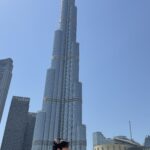 Rudi e a esposa em frente à fonte de Dubai, com o Burj Khalifa refletido atrás