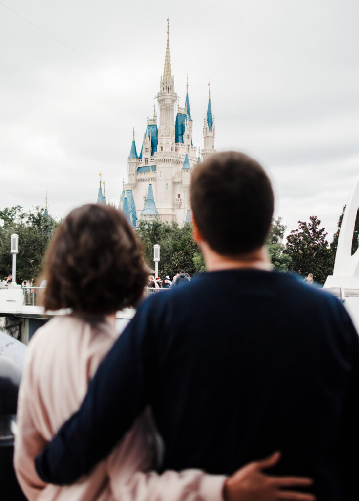 Casal abraçado de costas observando o Castelo da Cinderela durante ensaio fotográfico no Magic Kingdom