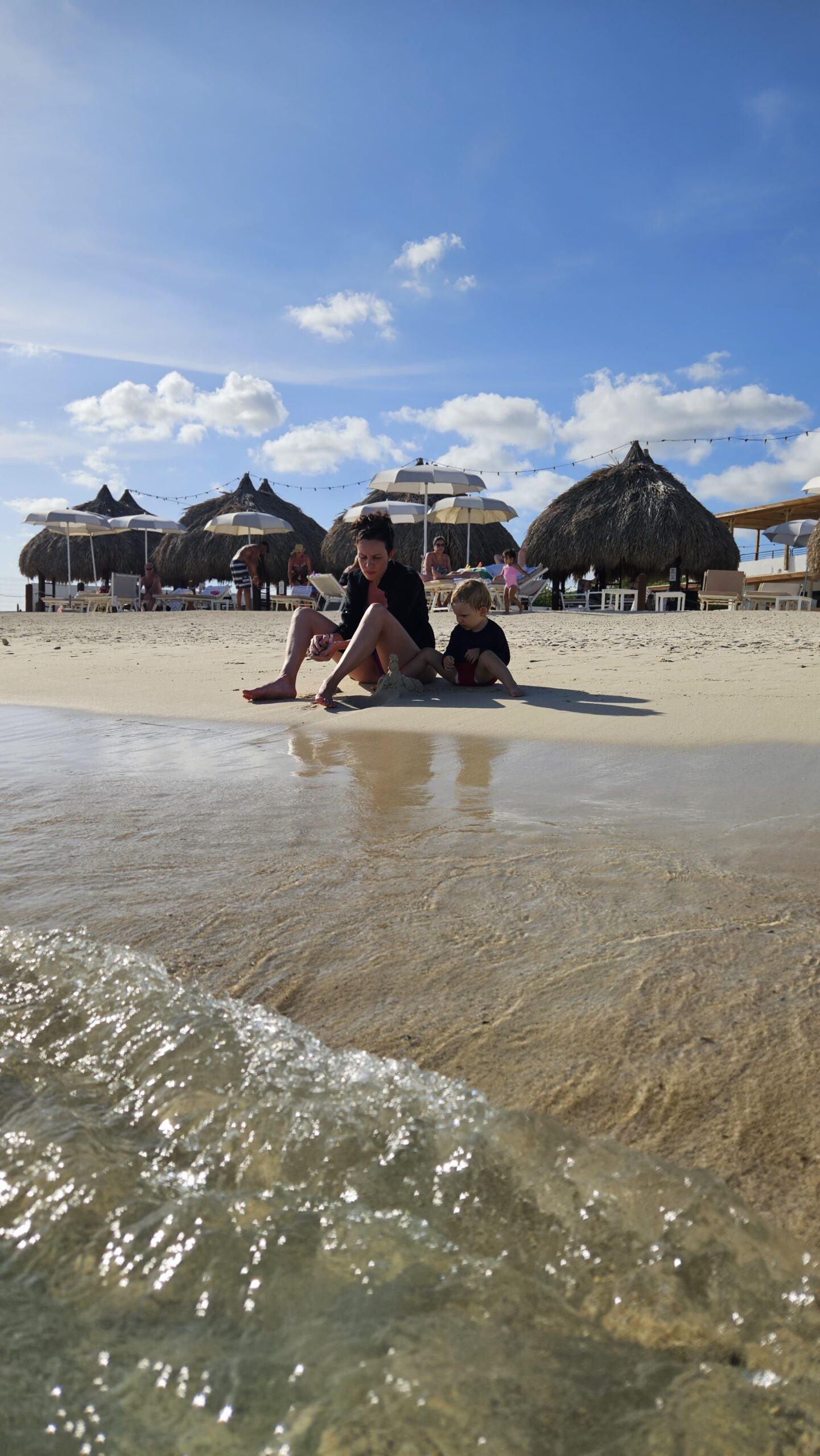 Família brincando na areia perto das cabanas de palha da Cas Abao Beach em Curaçao