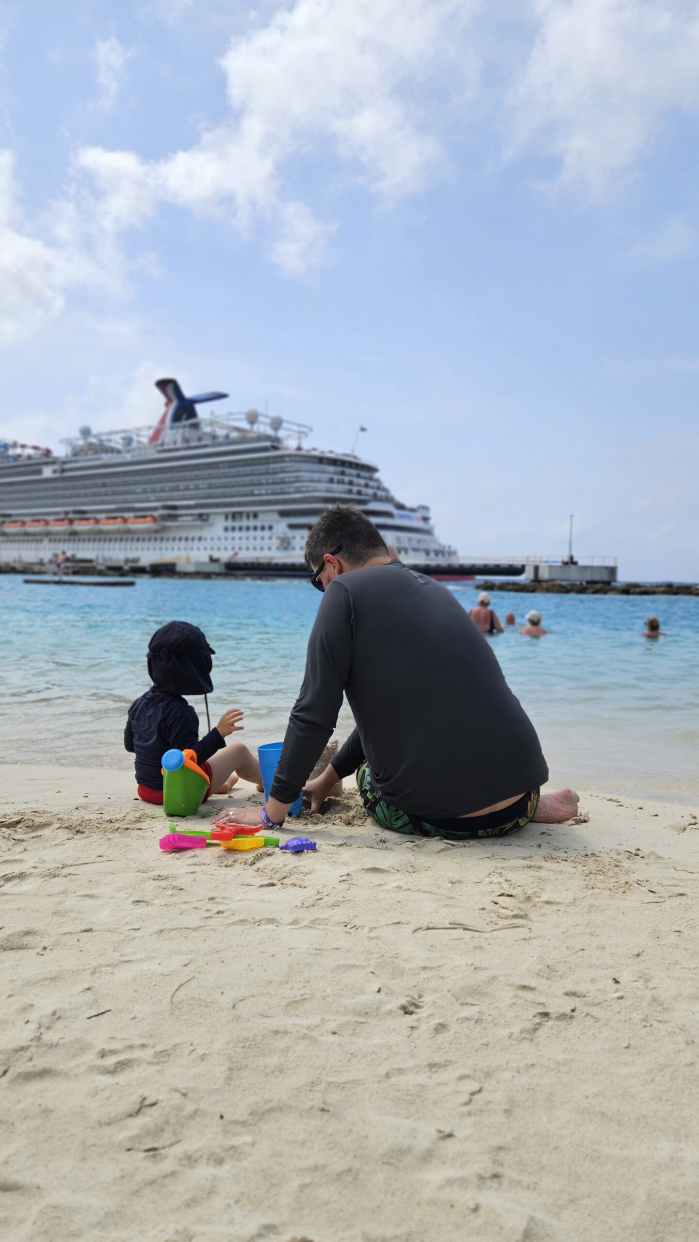 Rudi e Samuel brincando na areia em Curaçao, com navio de cruzeiro atracado ao fundo