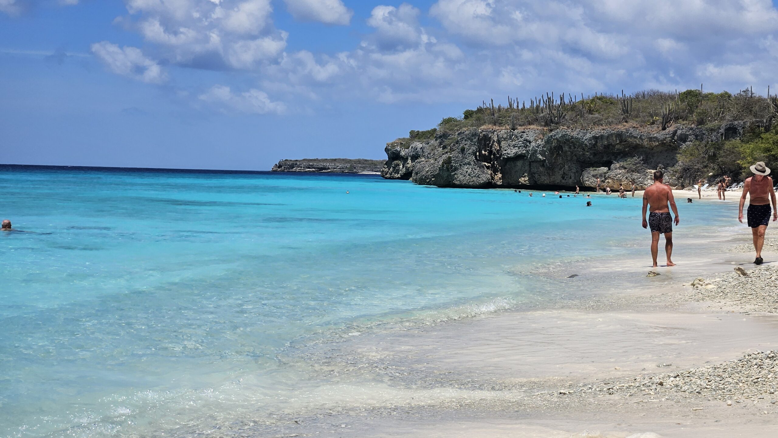 Praia de Curaçao com penhascos ao fundo, banhistas caminhando pela areia perto da água