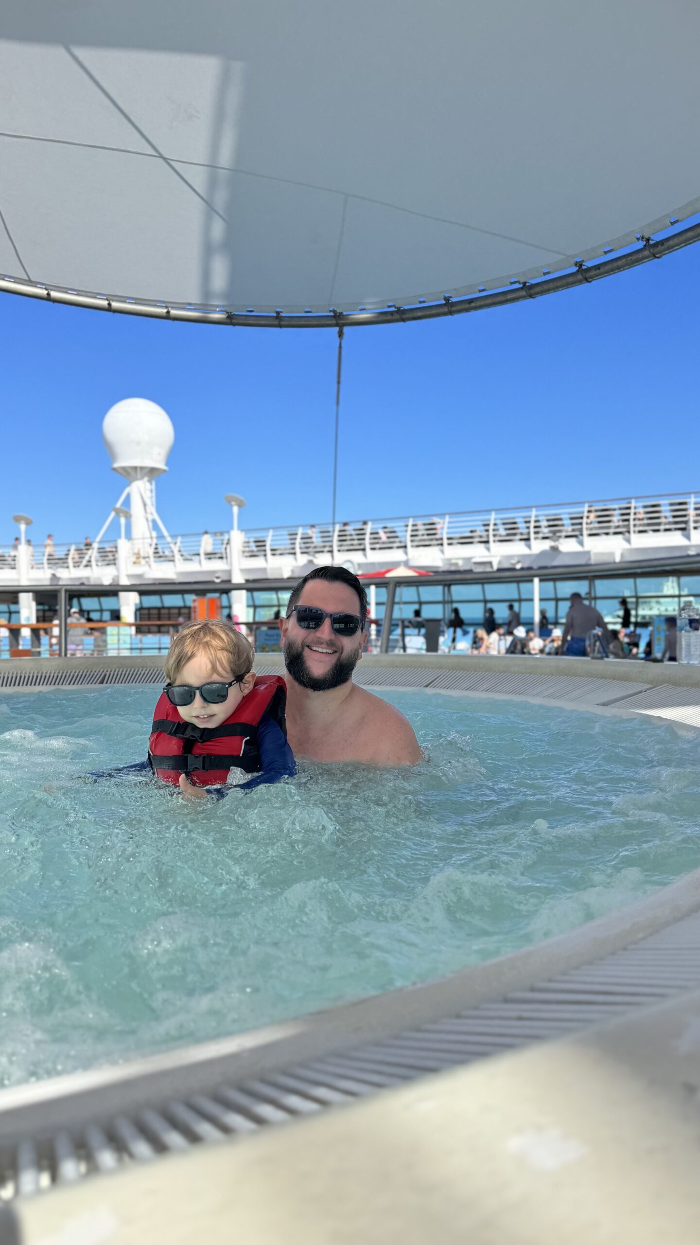 Piscina no deck do navio Royal Caribbean em dia ensolarado, com telão e estrutura do parque aquático ao fundo