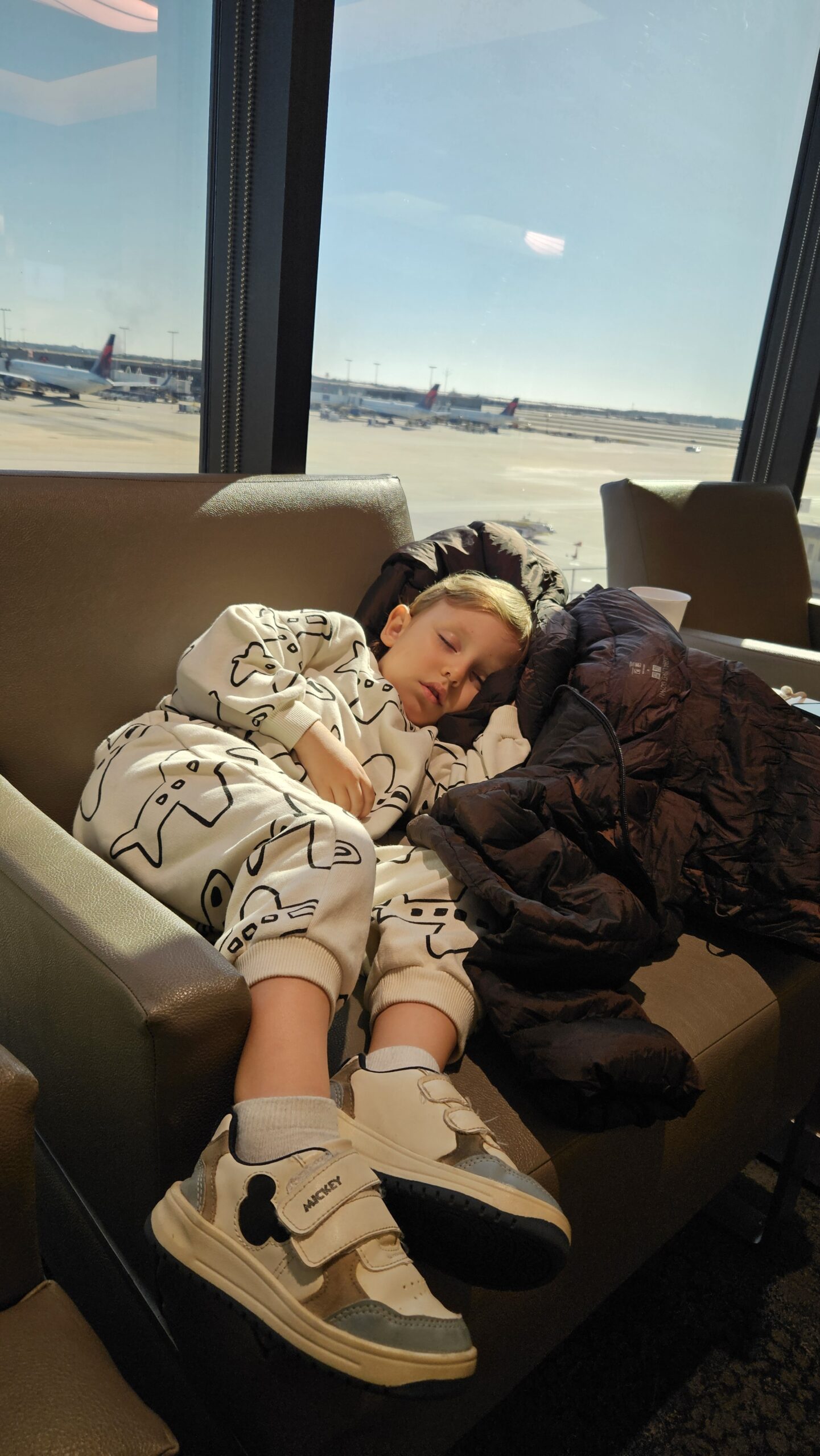 Samuel dormindo numa poltrona do Delta Sky Club em Atlanta com vista pro pátio do aeroporto