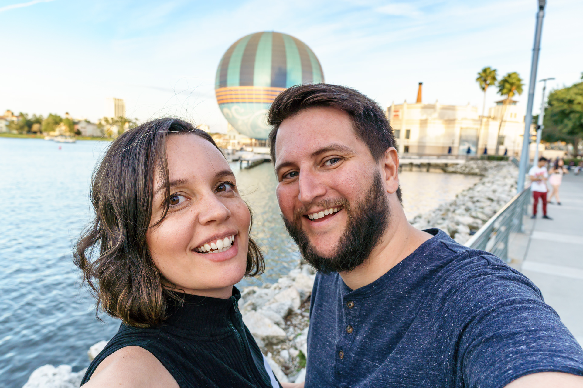 Casal em frente ao lago do Disney Springs, com o balão Characters in Flight ao fundo