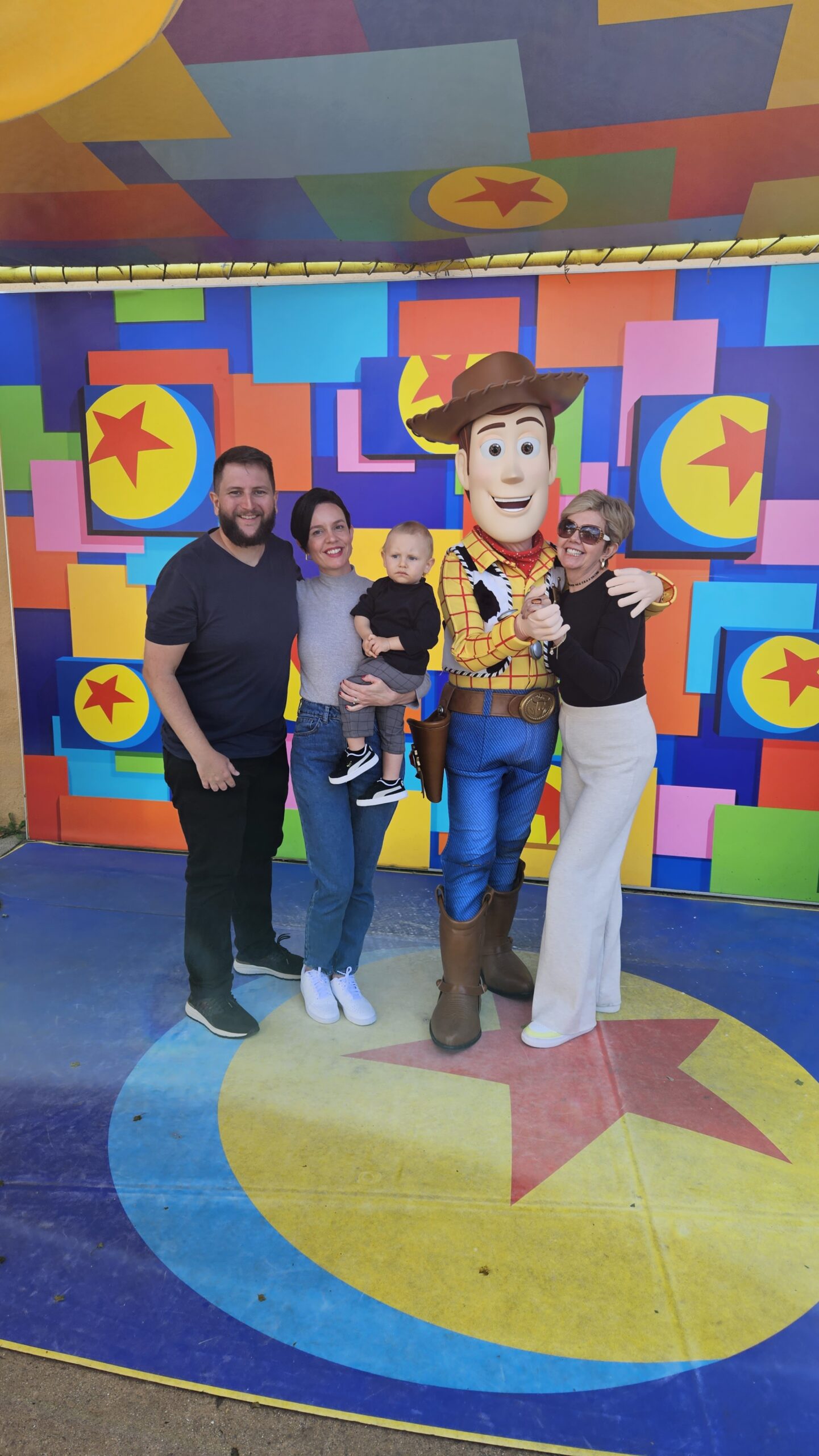 Avo com o bebe no colo em frente a estatua gigante do cachorro Slinky Dog na area de Toy Story