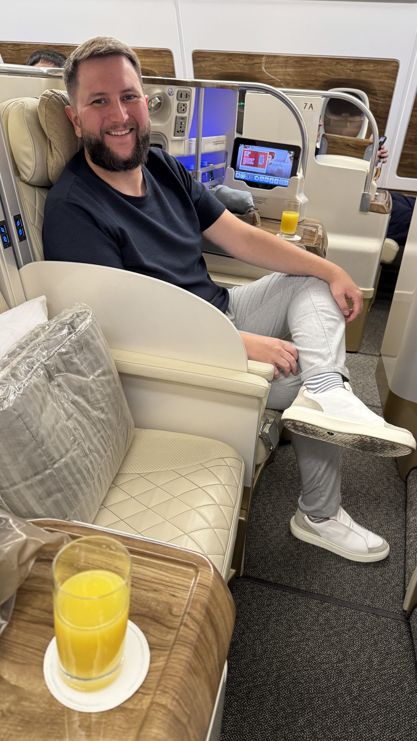 Rudi sentado na poltrona da executiva do A380 da Emirates com o suco de boas-vindas na mesinha