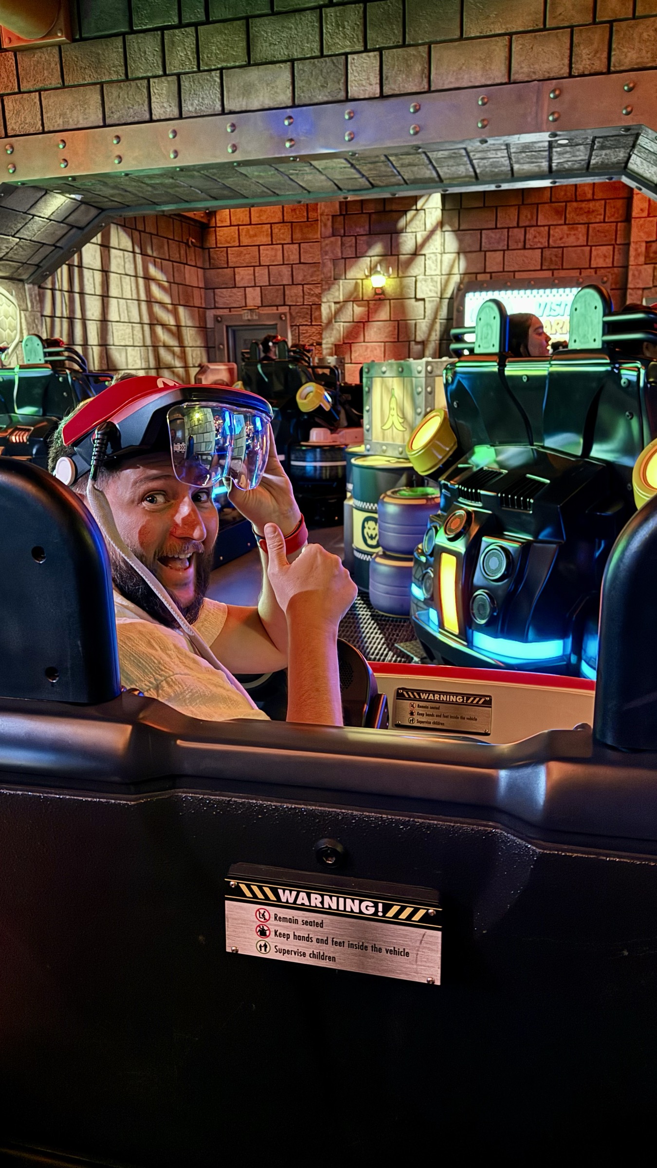 Rudi sentado no carrinho da atracao Mario Kart Bowser's Challenge usando os oculos de realidade aumentada acoplados ao chapeu do Mario