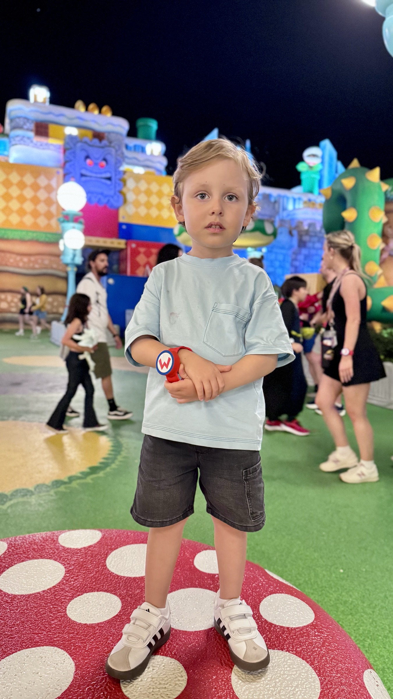 Casal sorrindo com o castelo do Super Nintendo World iluminado ao fundo, durante a noite no Epic Universe