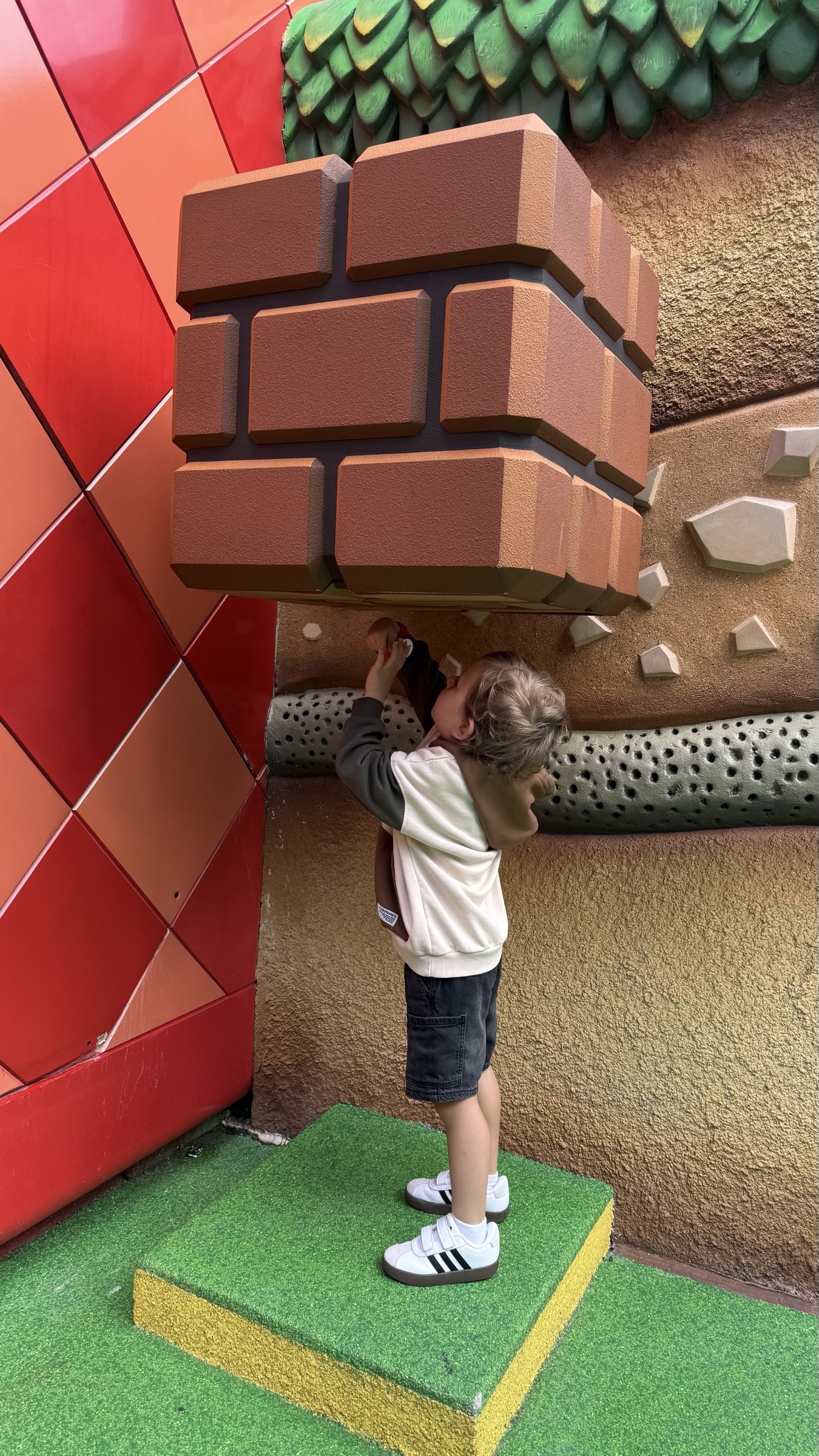 Samuel esticando o braco para bater em um bloco interativo de tijolos usando a pulseira Power-Up Band no Super Nintendo World