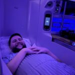 Rudi deitado na cama da executiva Emirates A380 com iluminação azul