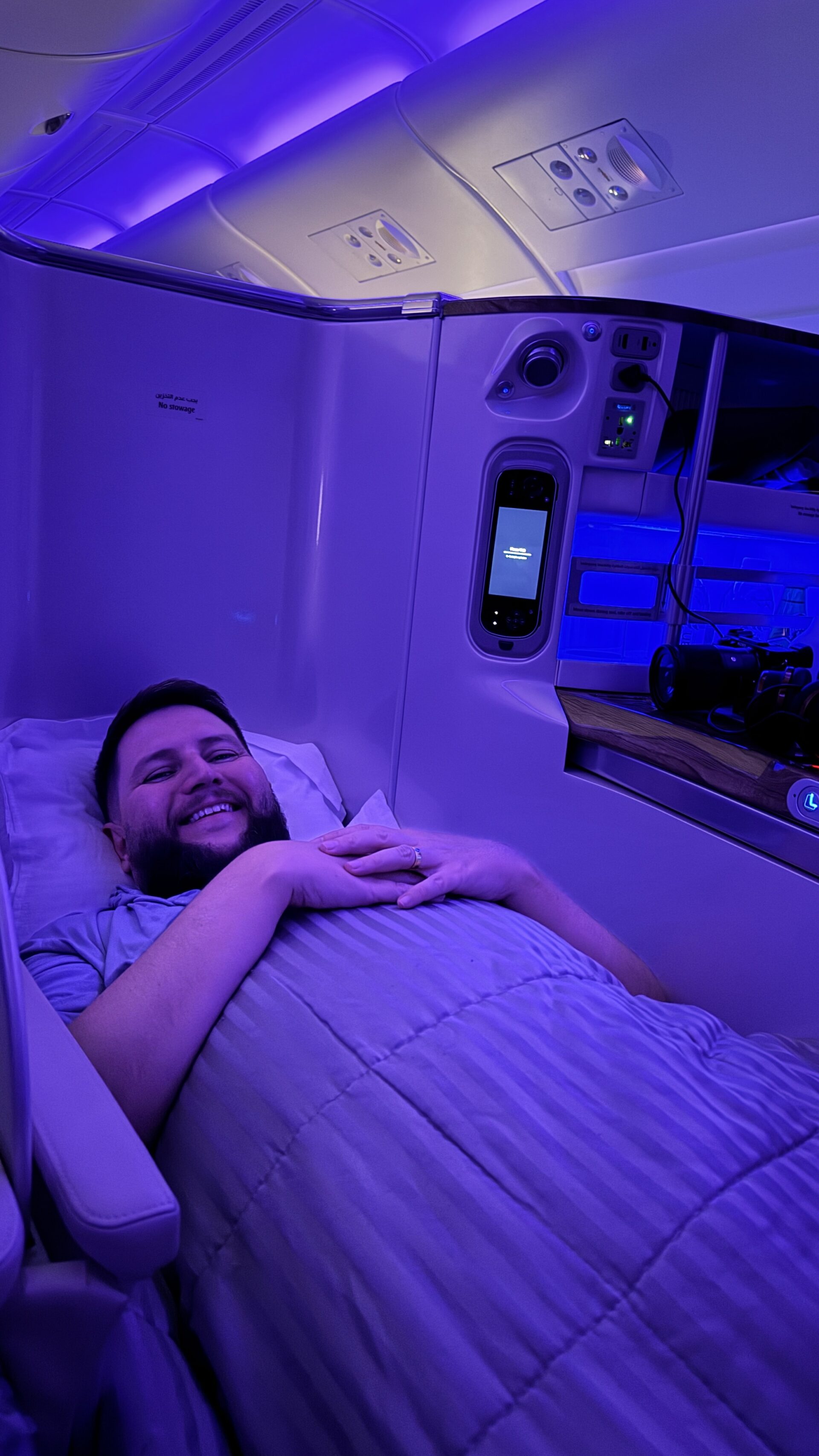 Rudi deitado na cama da executiva Emirates A380 com iluminação azul