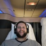 Rudi deitado na Qsuite da Qatar Airways com fone de ouvido