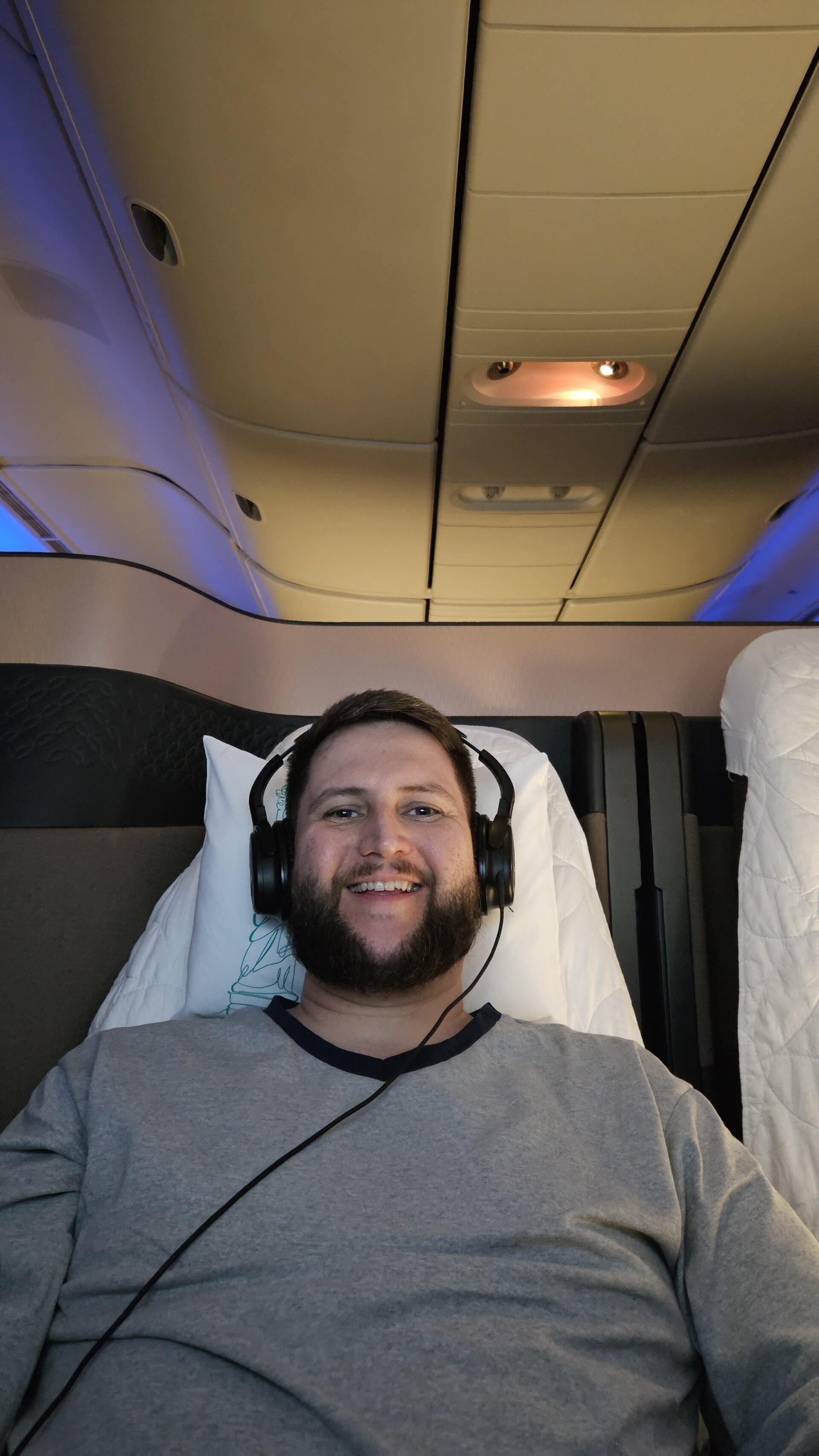 Rudi deitado na Qsuite da Qatar Airways com fone de ouvido