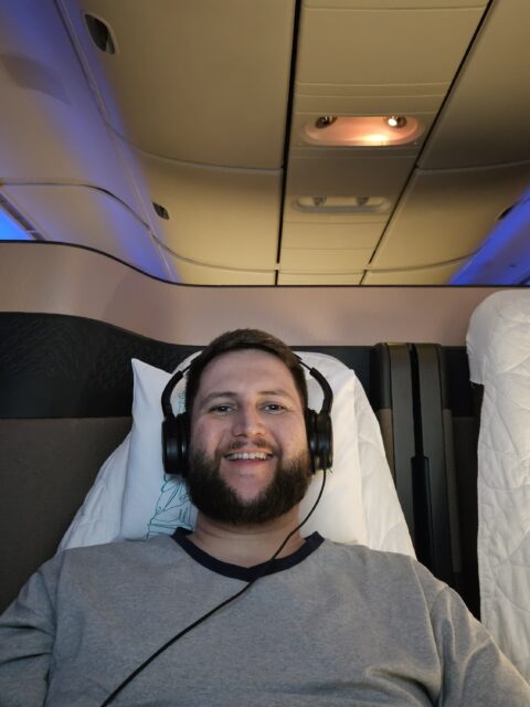 Rudi deitado na Qsuite da Qatar Airways com fone de ouvido