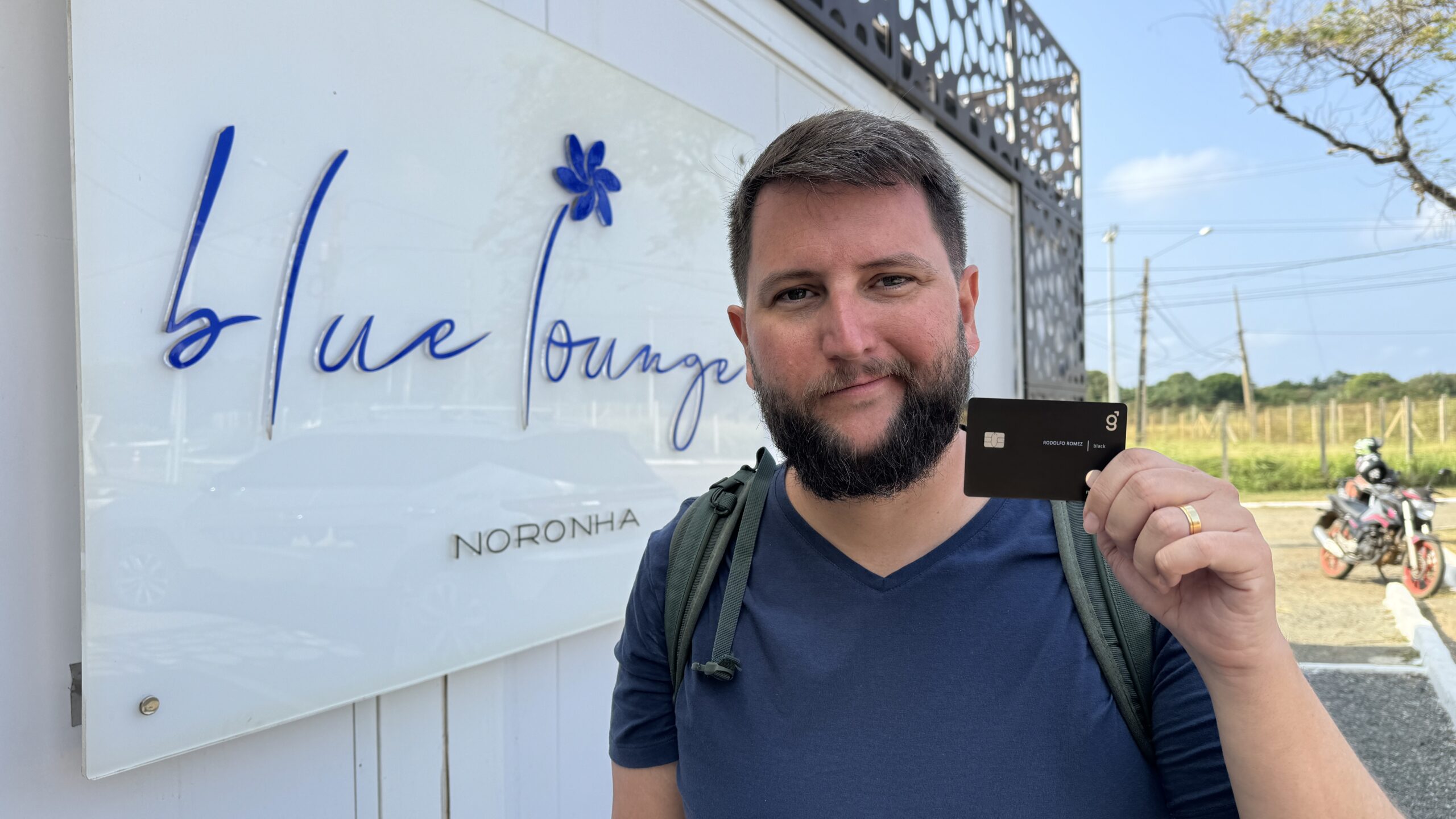 Homem em frente à fachada da Blue Lounge no Aeroporto de Fernando de Noronha, segurando o cartão usado para acesso