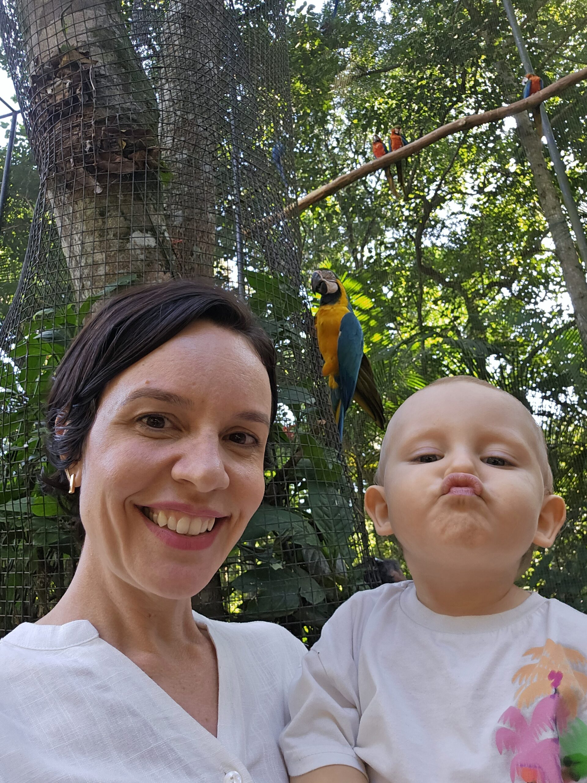 Mãe e Samuel dentro do viveiro das araras no Parque das Aves, com arara-azul ao fundo