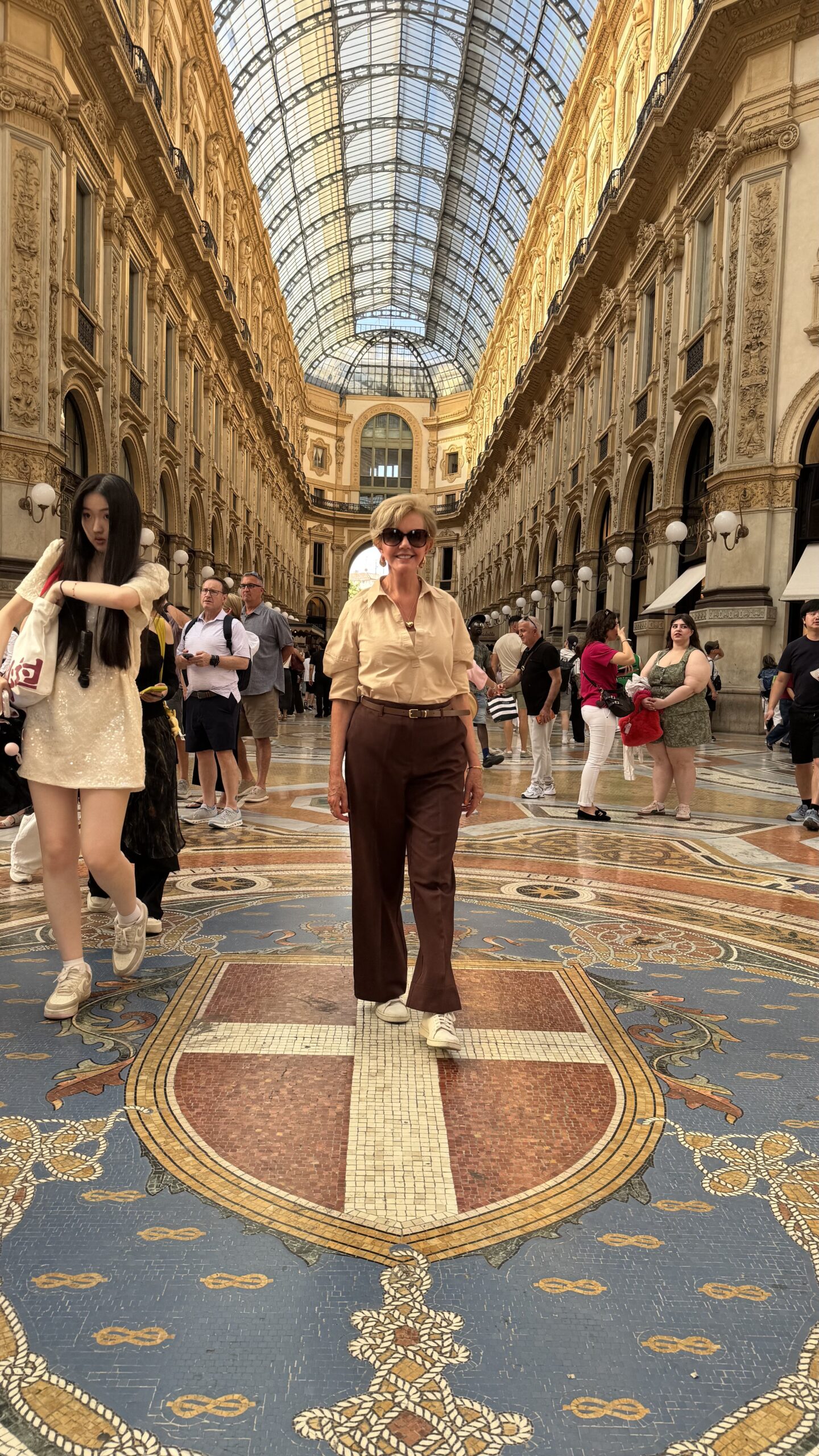 Mulher em pé sobre o mosaico central da Galleria Vittorio Emanuele II, com a cúpula de vidro ao fundo