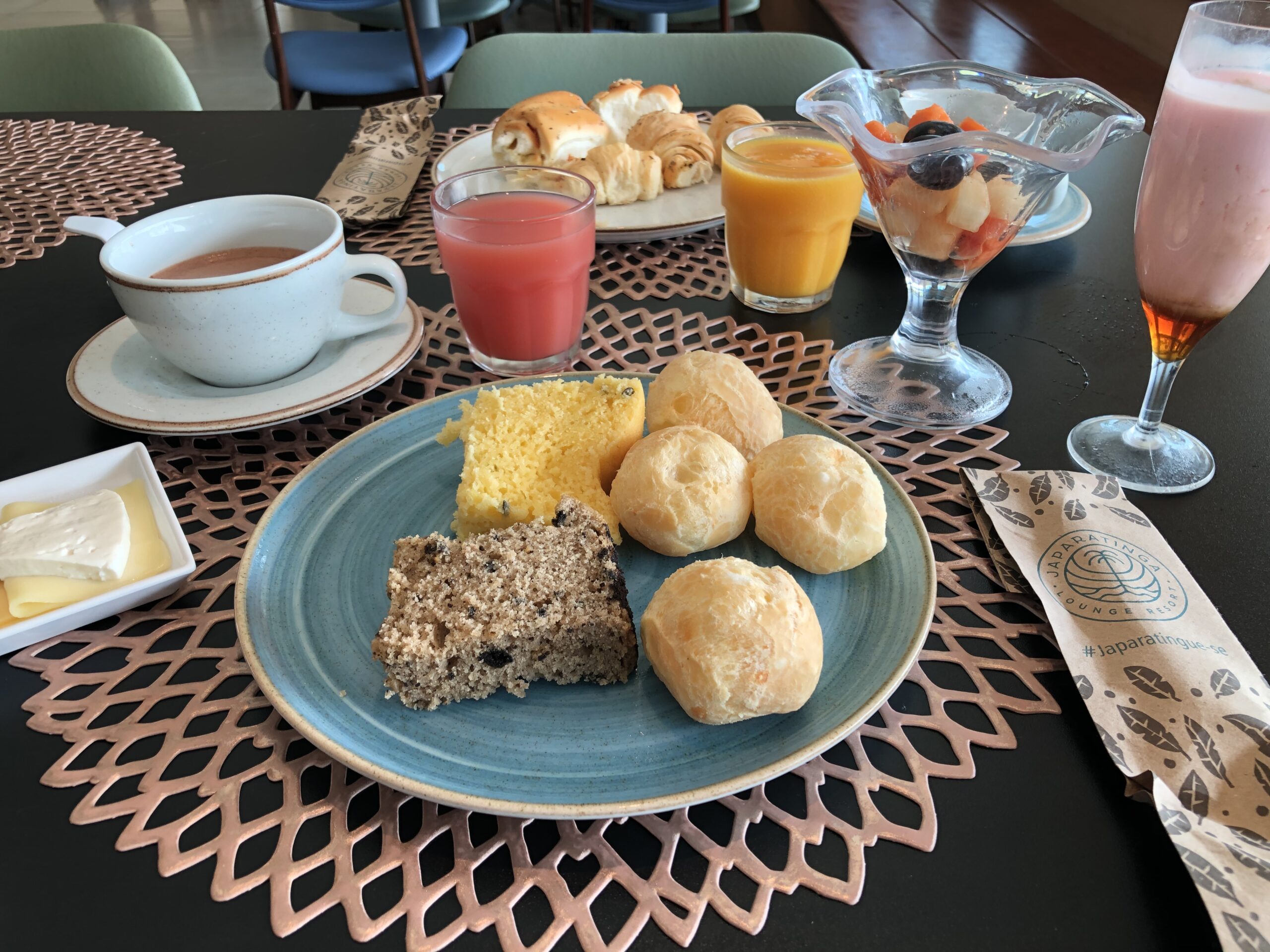 Mesa de café da manhã no Japaratinga Lounge Resort com pão de queijo, bolos regionais, sucos naturais e espumante
