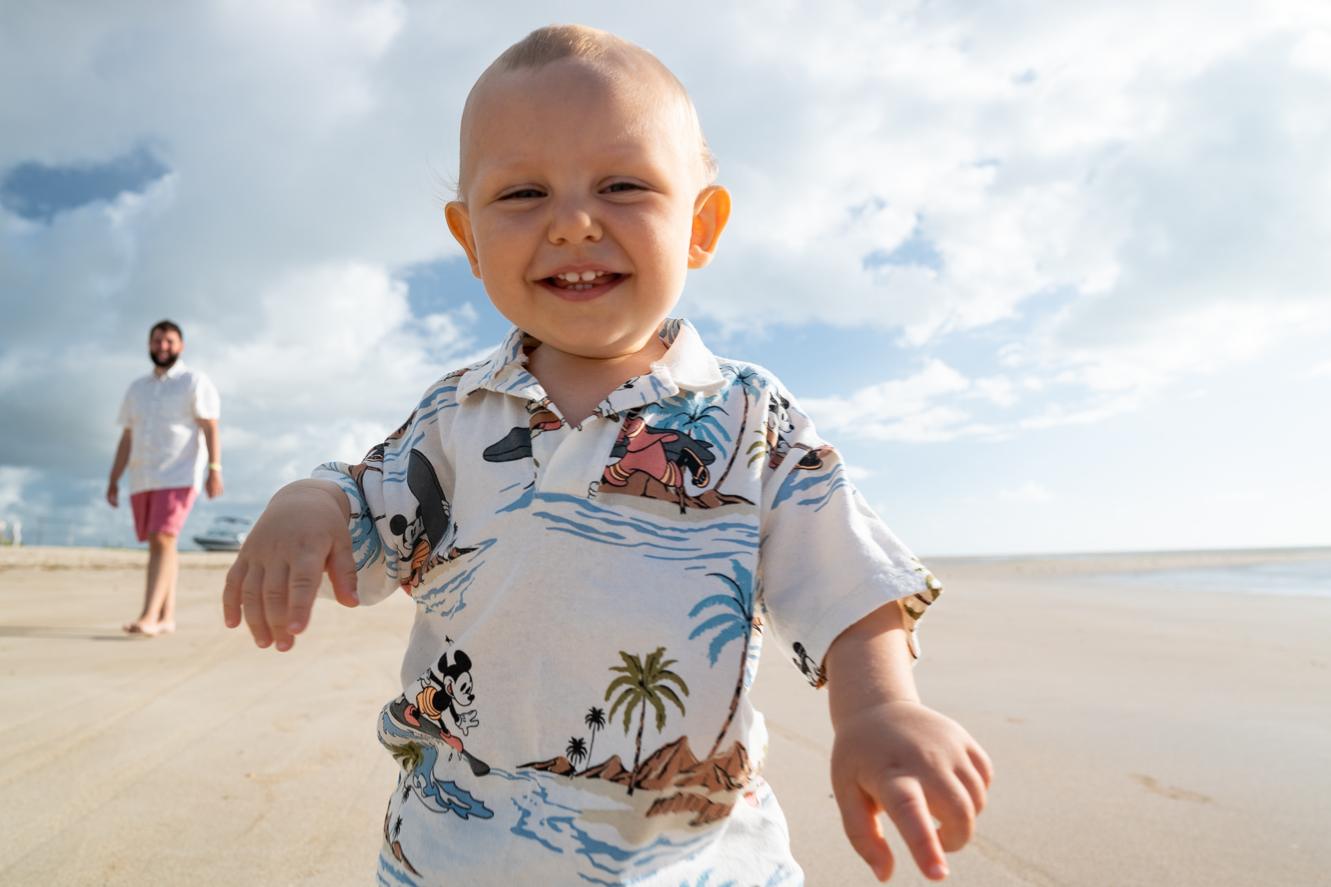 Samuel sorrindo na Praia do Salgado perto do Japaratinga Lounge Resort, com o pai ao fundo