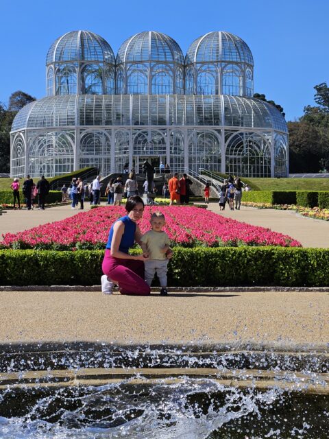 Familia em frente ao canteiro de flores rosa com a estufa de ferro e vidro do Jardim Botanico de Curitiba ao fundo