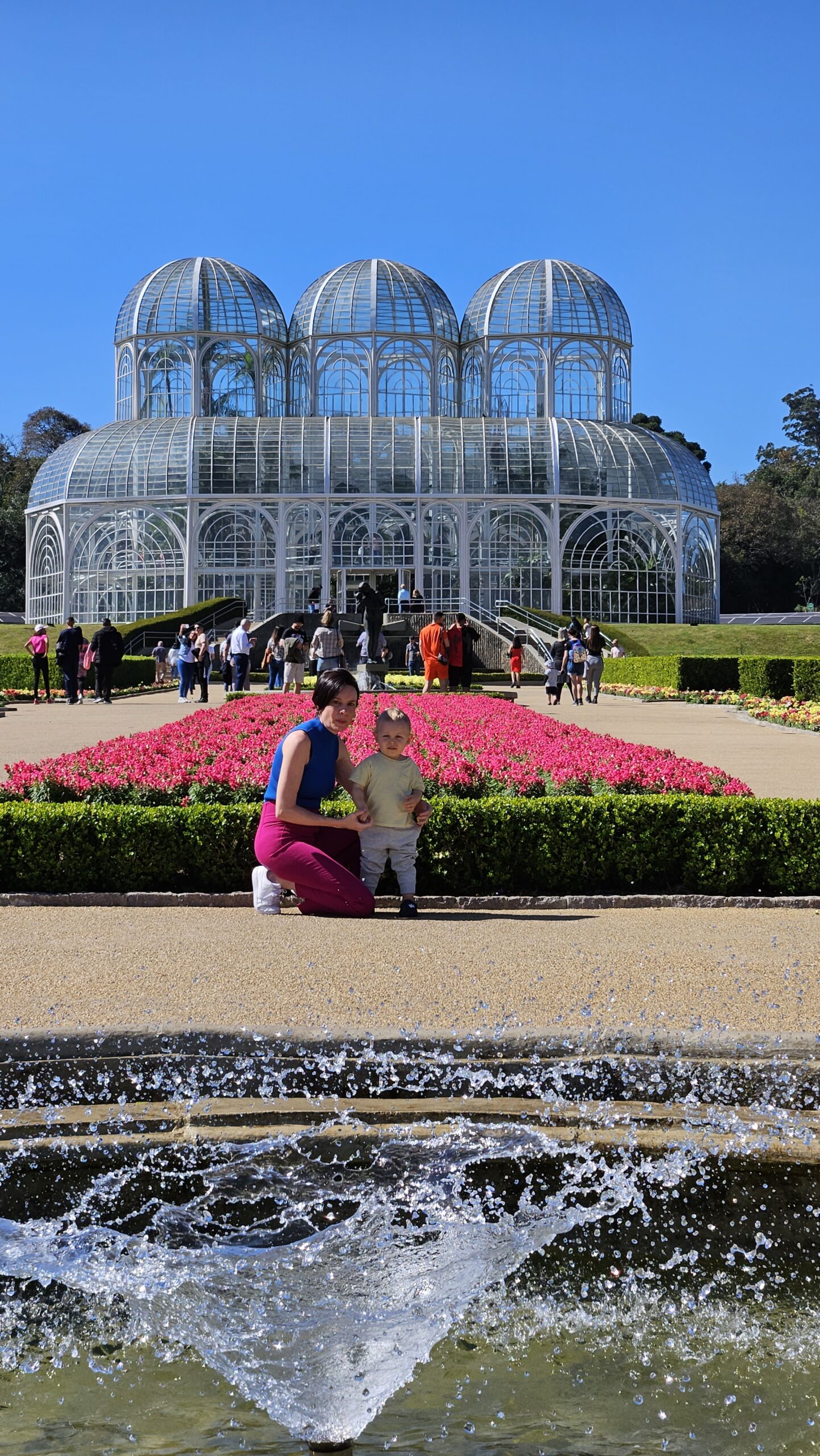 Família em frente ao canteiro de flores rosa com a estufa de ferro e vidro do Jardim Botânico de Curitiba ao fundo