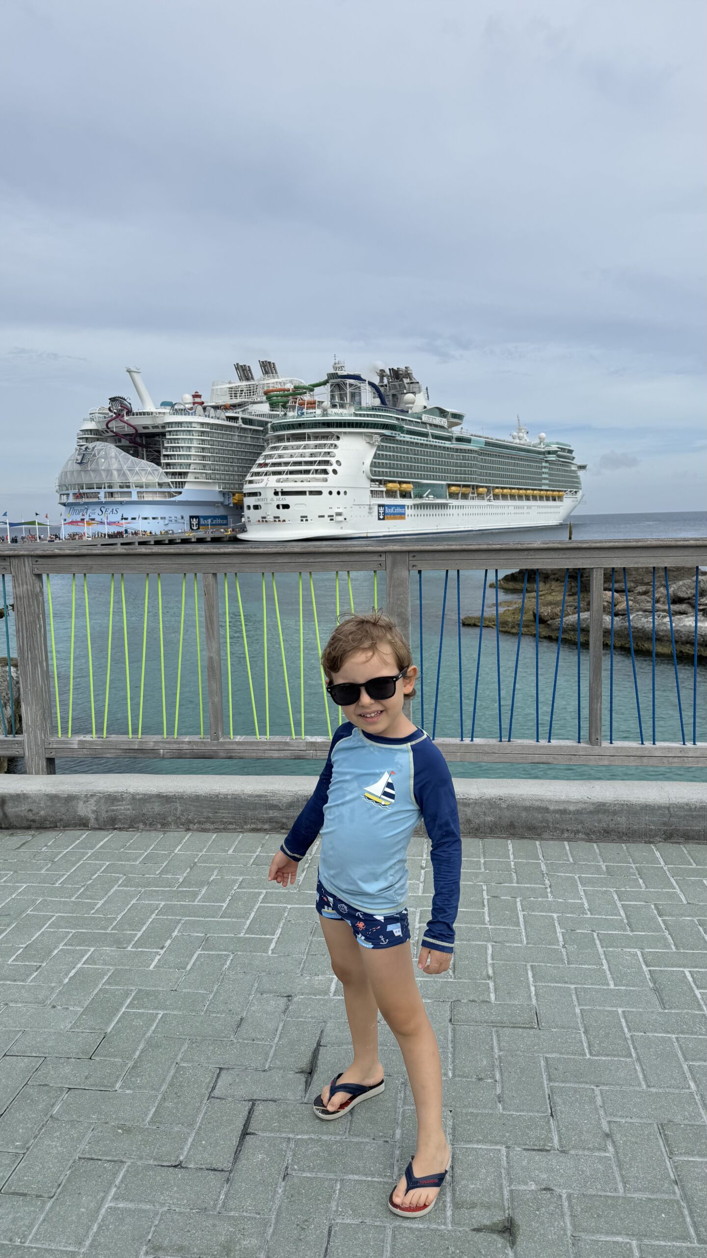 Criança de óculos escuros na ilha privativa da Royal Caribbean nas Bahamas, com os navios ao fundo