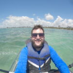 Rudi de caiaque na orla de Maceió com o skyline ao fundo