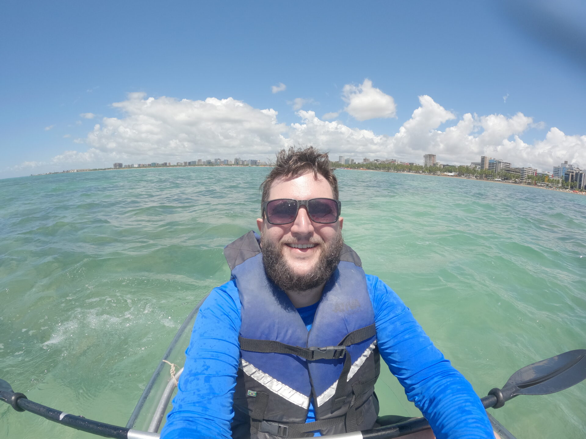 Rudi de caiaque na orla de Maceió com o skyline ao fundo