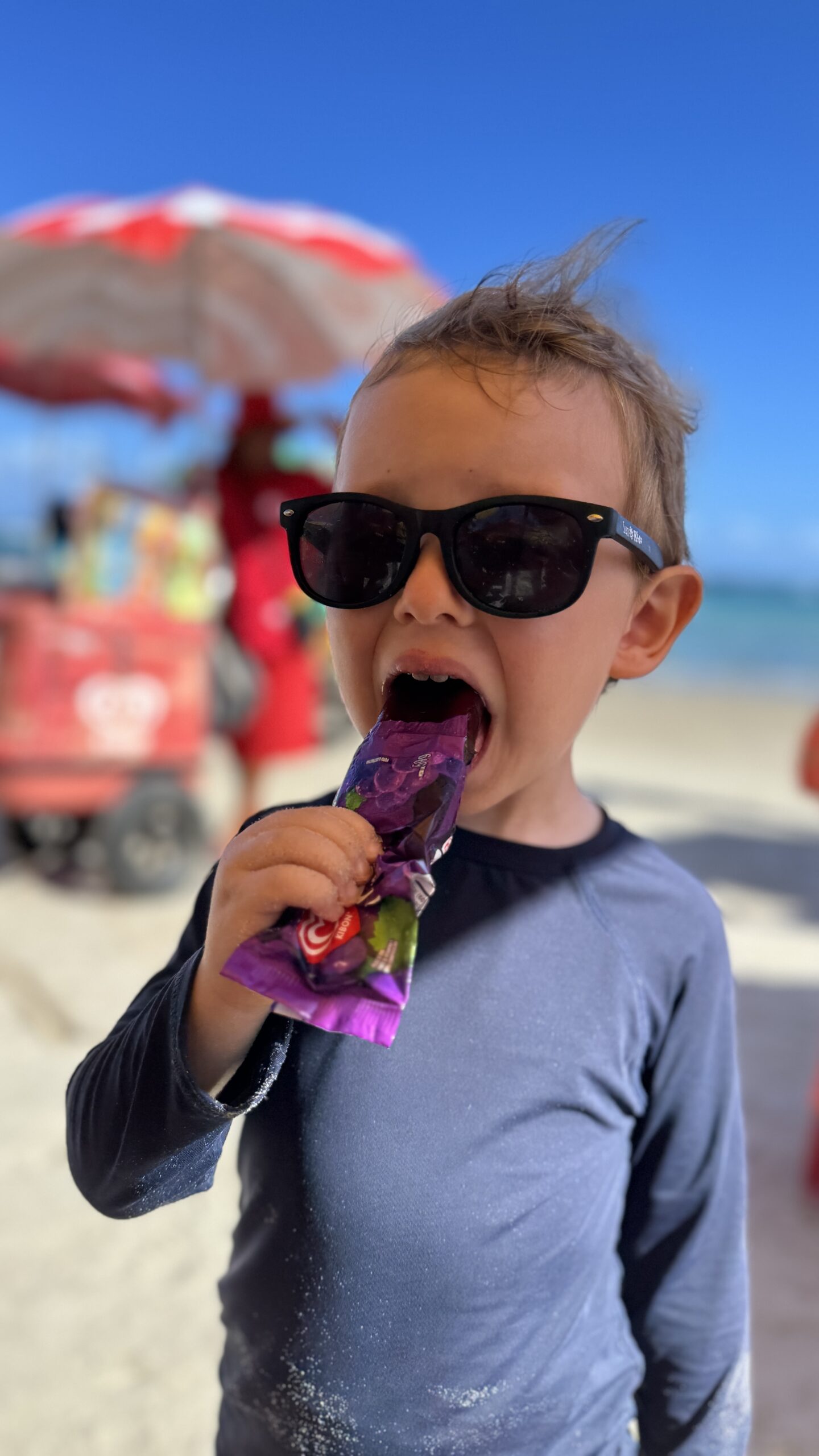 Samuel de óculos escuros comendo picolé de uva na Praia de Pajuçara