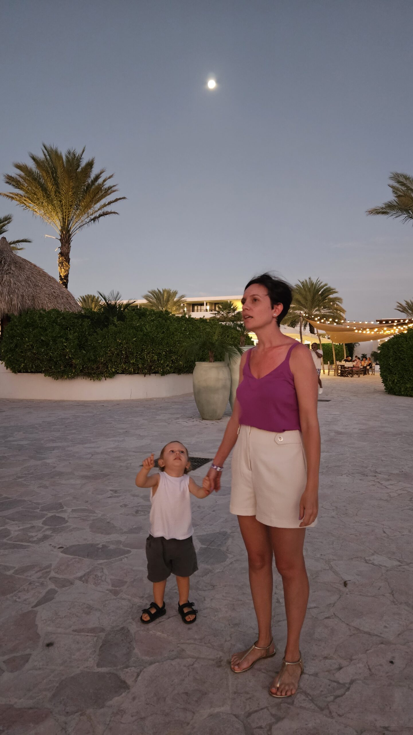 Família passeando à noite pelo Mangrove Beach Resort em Curaçao, com a lua cheia no céu