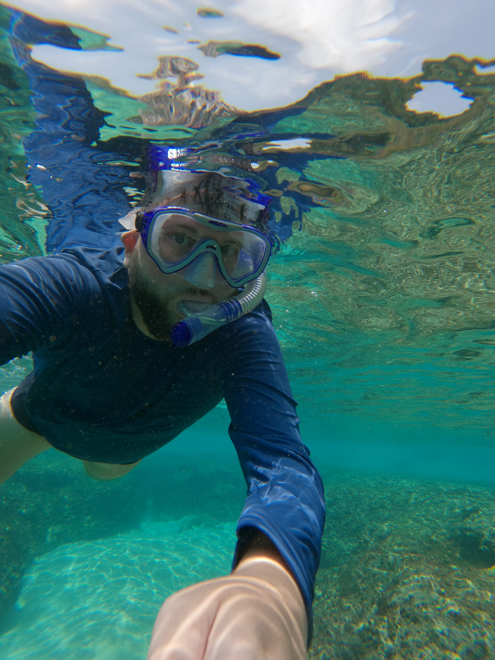 Pessoa fazendo snorkel em água cristalina em Fernando de Noronha, com o fundo do mar visível