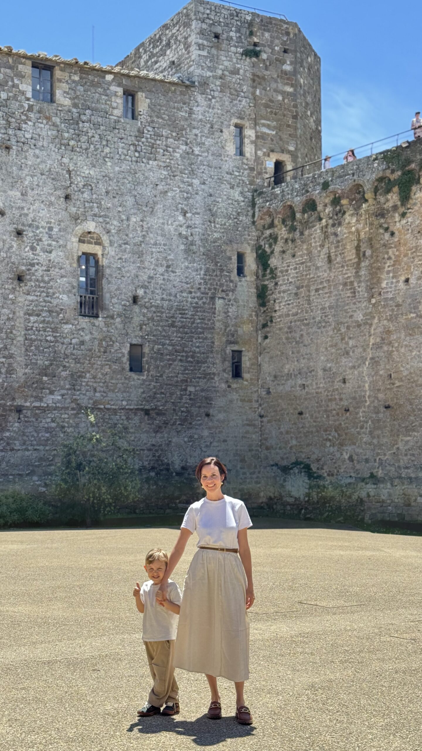 Mãe e filho sentados em banco dentro da Fortezza de Montalcino, com muralha de pedra ao fundo