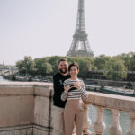 Casal com o bebê no colo posando em frente a bicicletas com a Torre Eiffel ao fundo, em ensaio fotografico profissional em Paris